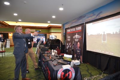 Two men in suits using a virtual shooting simulator at a conference.