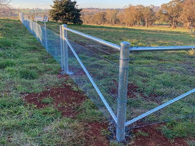 Newly installed metal mesh fence spanning across a grassy field.