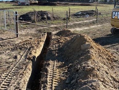 Excavated trench with nearby dirt piles and construction machinery tracks.