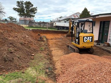 A yellow CAT excavator digging soil near a house under cloudy sky.