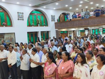 Large group gathered indoors, attentive and solemn.