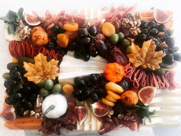 Colorful autumn-themed charcuterie board with fruits, nuts, and cheese.
