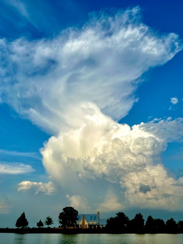 Large, dramatic cloud formation over a lakeside house.