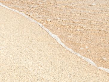 Gentle ocean wave washing onto a sandy beach shore.