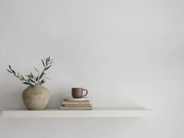 Minimalist shelf with a rustic vase, books, and a coffee cup.