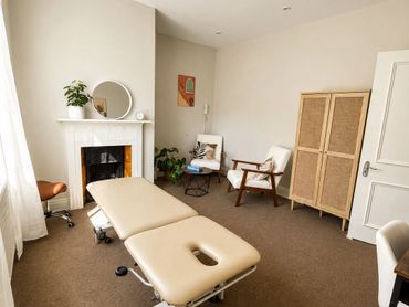 Bright and cozy therapy room with a treatment table and comfortable seating.