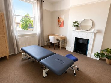 Bright, minimalist therapy or massage room with a black table and natural decor.