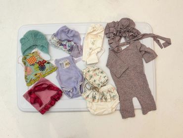Newborn baby clothes and accessories arranged on a white tray.