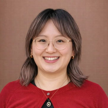 Smiling woman with glasses and shoulder-length hair in red and black attire.