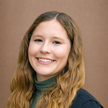 Smiling young woman with long wavy hair against a plain background.