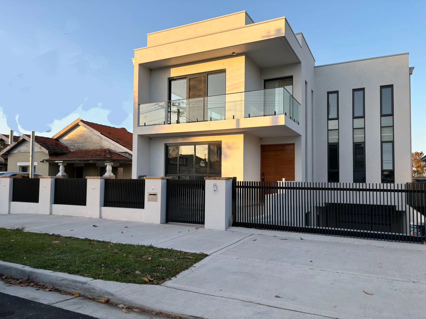 Modern two-story house with glass balcony and black fence under clear sky.