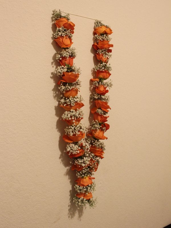 Orange color roses and baby’s breath stringed together to make a garland hangin on a wall