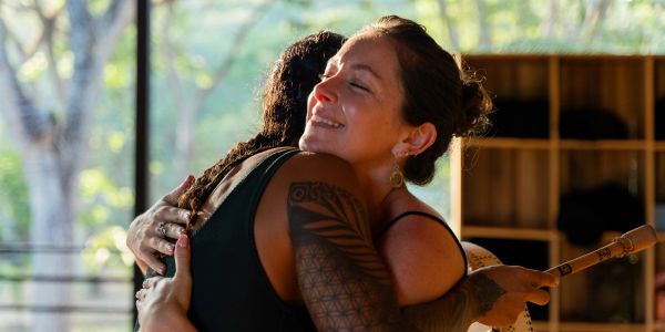 Two women warmly hugging indoors near a window.