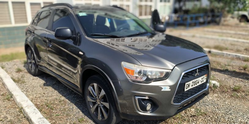 Gray Mitsubishi SUV parked on a gravel lot in daylight.