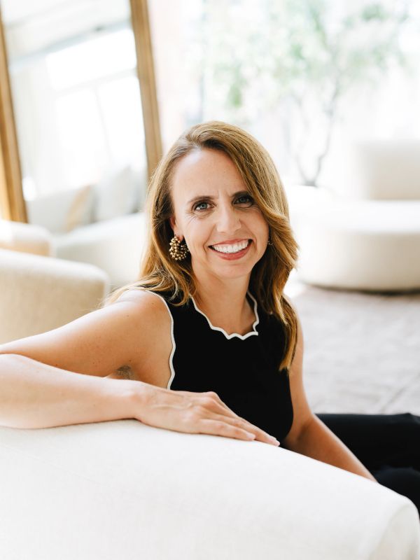 Smiling woman in black sleeveless top sitting on a white couch.