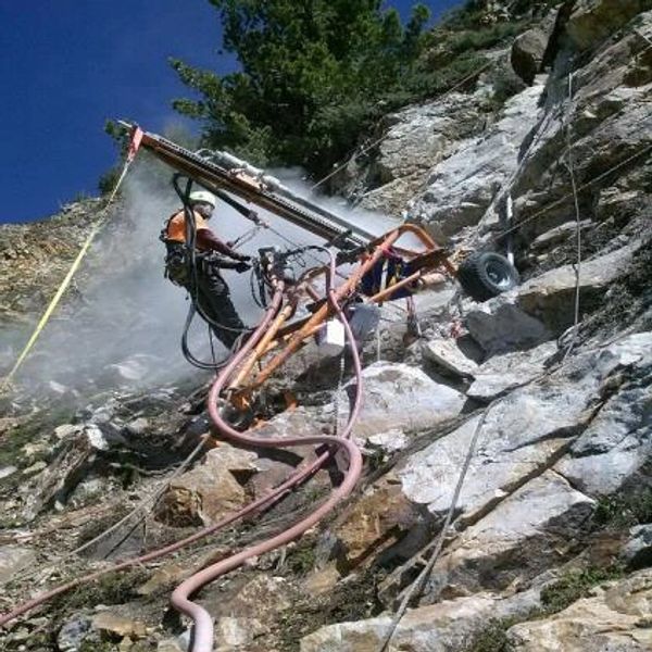 Worker operating drilling equipment on a rocky cliff face.