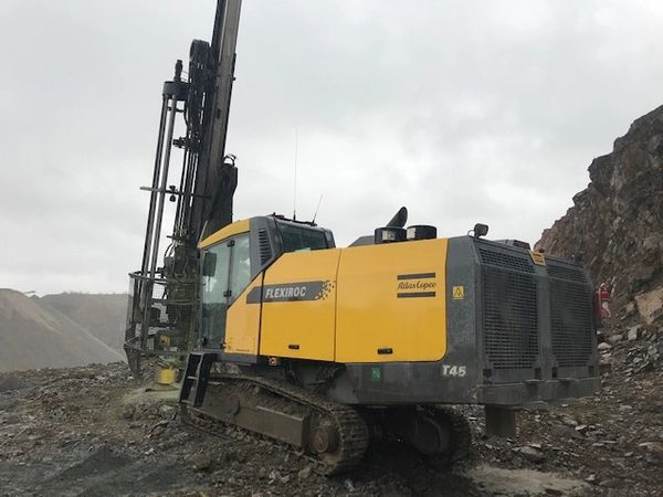 Yellow and black drilling machine on rocky terrain under a cloudy sky.