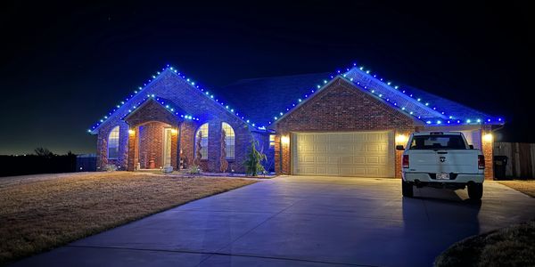Brick house decorated with blue and white Christmas lights at night.