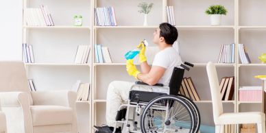 Man in wheelchair cleaning a bookshelf.