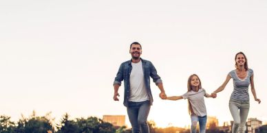 Happy family holding hands outdoors during sunset.