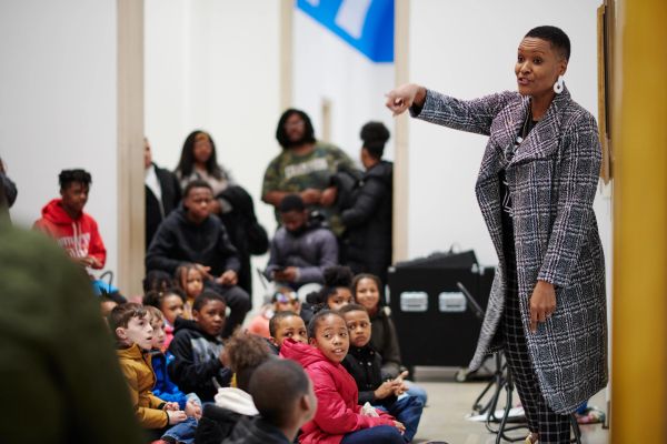 Woman speaks to attentive children in a school setting.