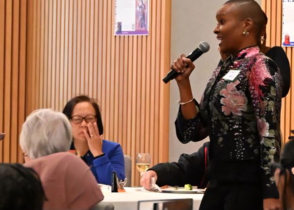 Woman speaking with a microphone at an indoor event.
