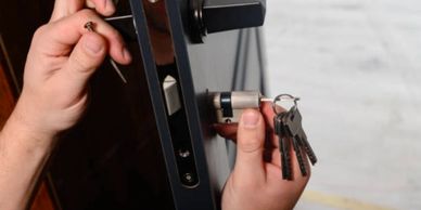 A person installing or repairing a lock with multiple keys in hand.