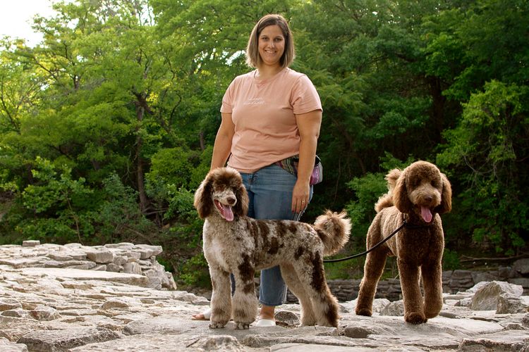 Goldendoodle breeder standing with her two standard size dogs. They are chocolate and merle