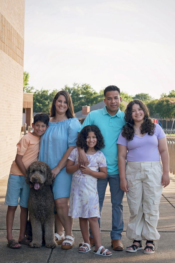 A biracial family of 5 are standing with their chocolate standard goldendoodle all are smiling