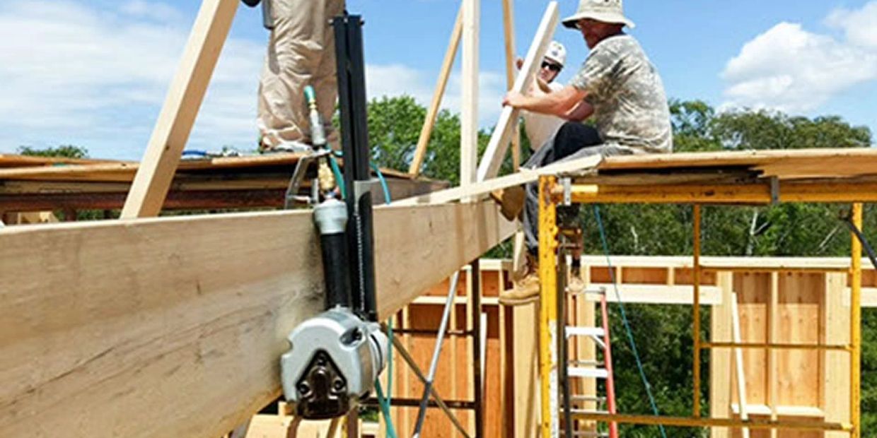 Construction workers assembling wooden framework on scaffolding under a clear sky.