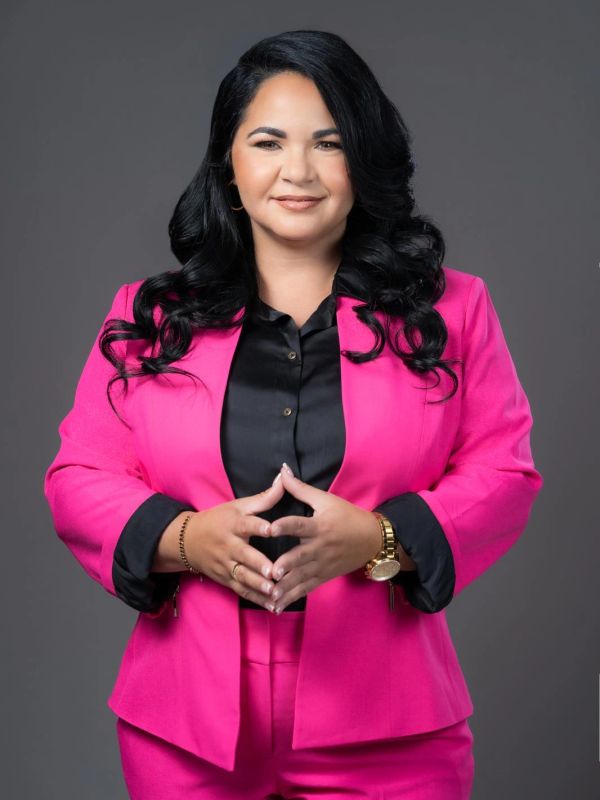 Mujer sonriente con traje rosa y blusa negra.