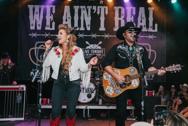 Country duo performing live on stage with guitars and western outfits.