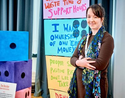 Ria stands in front of some of her artwork: slogans about support packages and large dice