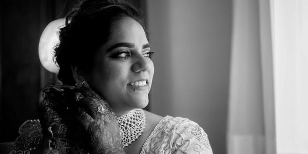 Black and white portrait of a smiling bride looking out the window.