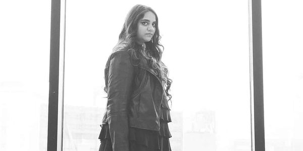 Woman in black leather jacket standing by window.