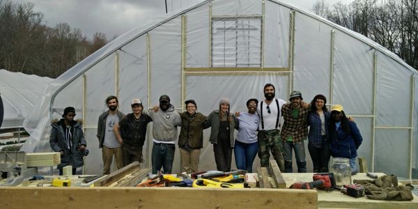 Group of diverse people standing in front of a greenhouse with construction tools.