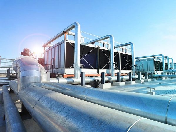 Industrial HVAC cooling system with large metal pipes under blue sky.
