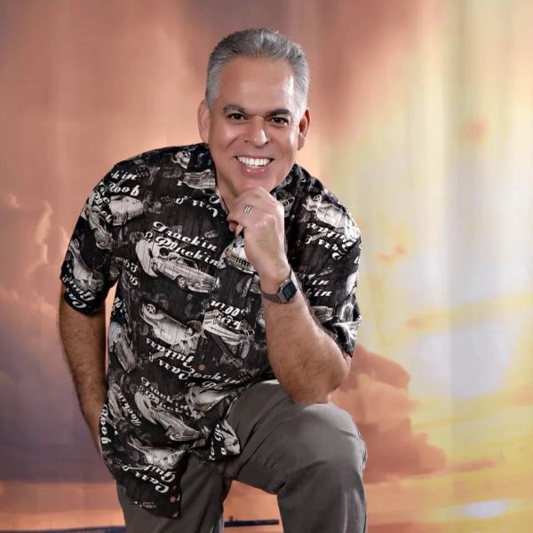 Smiling man posing with hand on chin against a warm background.