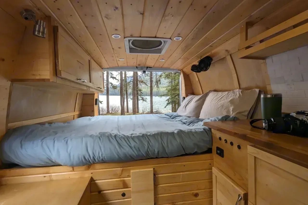 Cozy wooden camper van interior with a bed and nature view.