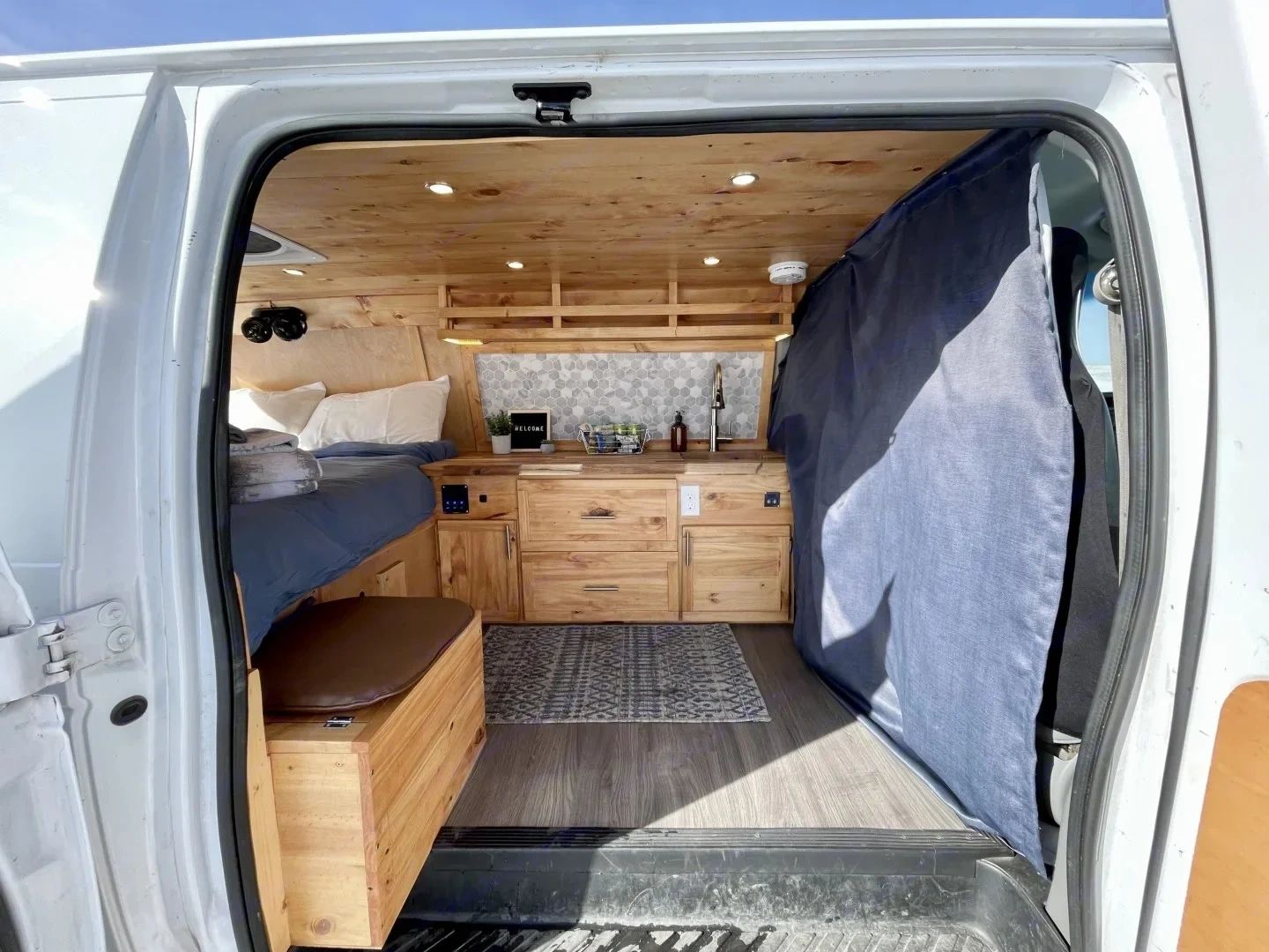 Cozy wooden camper van interior with bed, kitchenette, and storage.
