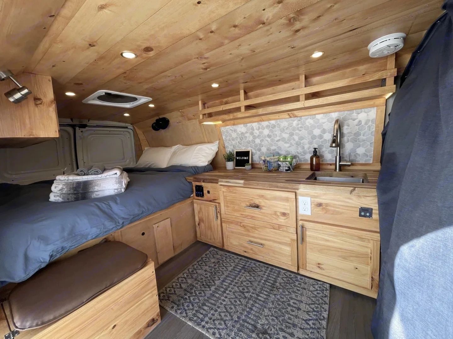 Cozy wooden interior of a camper van with bed and kitchenette.