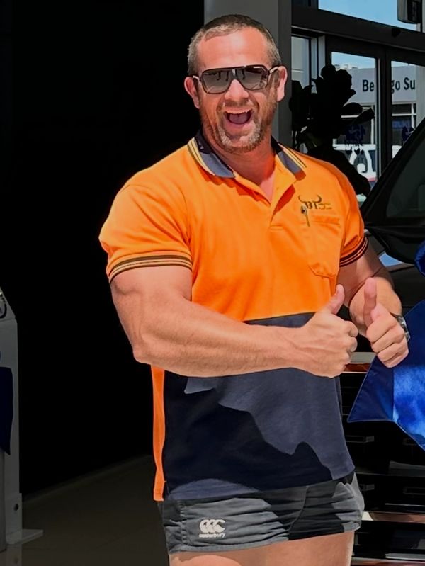 Man in orange shirt and sunglasses giving thumbs up with a big smile.