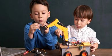 Two boys building and programming a robotic vehicle with a mechanical arm.