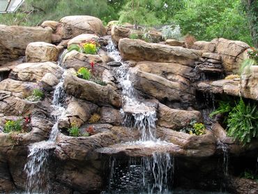 Multiple cascading waterfalls on artificial rock structure. Planter pockets, texture, and dimension.