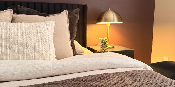 Cozy bedroom corner with plush pillows and golden lamp.