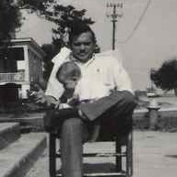 A man sitting on a chair holding a child outdoors in a black-and-white photo.