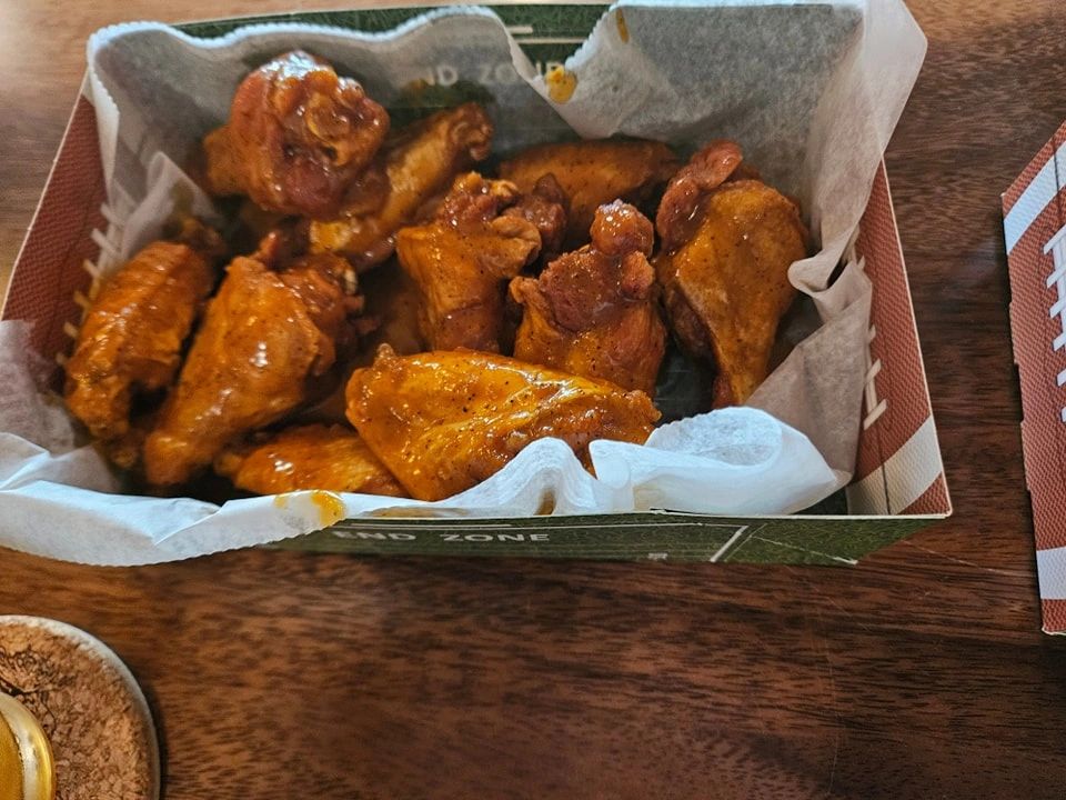 A box of saucy chicken wings on a wooden table.