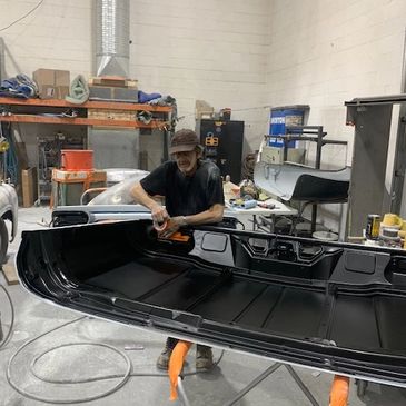 Man polishing a large black car part in a workshop.