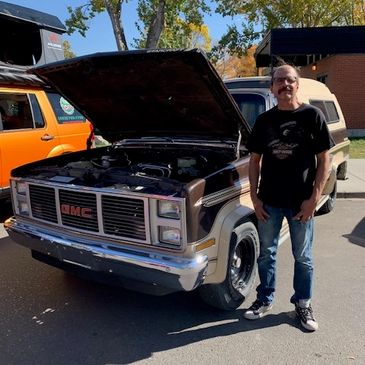 Man standing beside a vintage GMC truck with its hood open.