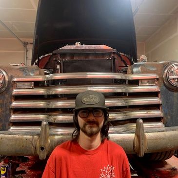 Person wearing a hat and glasses in front of an old vehicle.
